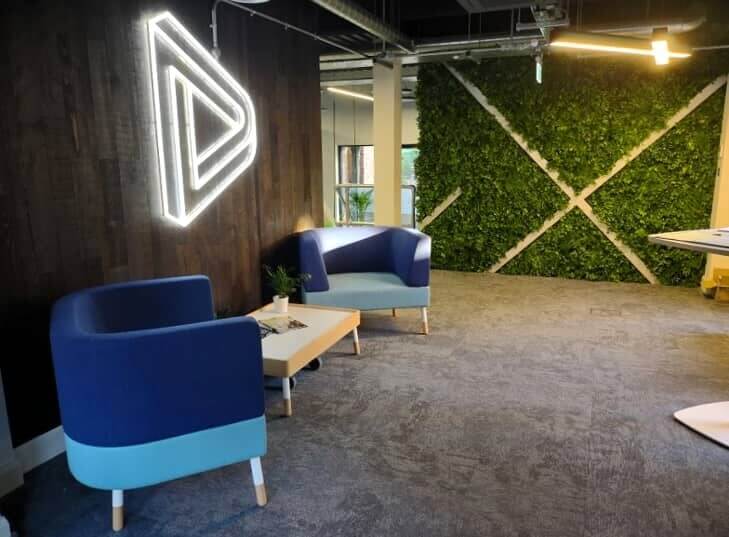 An office space with a wall-mounted light up logo and grass accent wall.